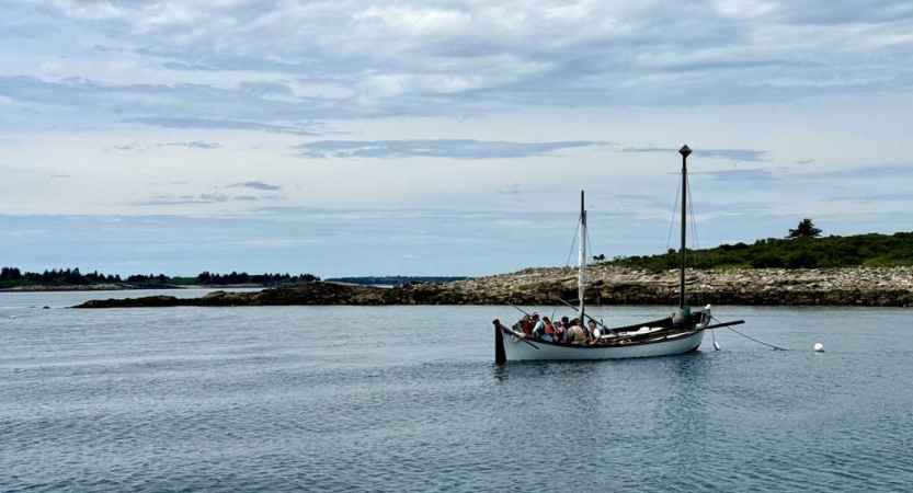 From a distance, a sailboat floats on water under a blue sky.